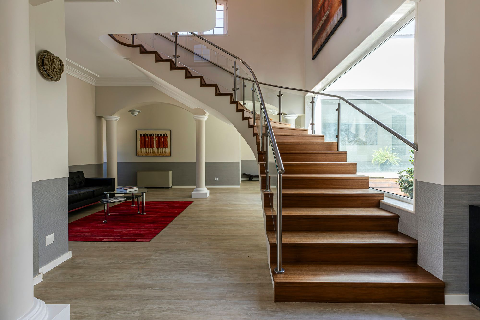 Curved wooden staircase, black sofa and red rug in the stair hall at Cascais Vacation, Cascais
